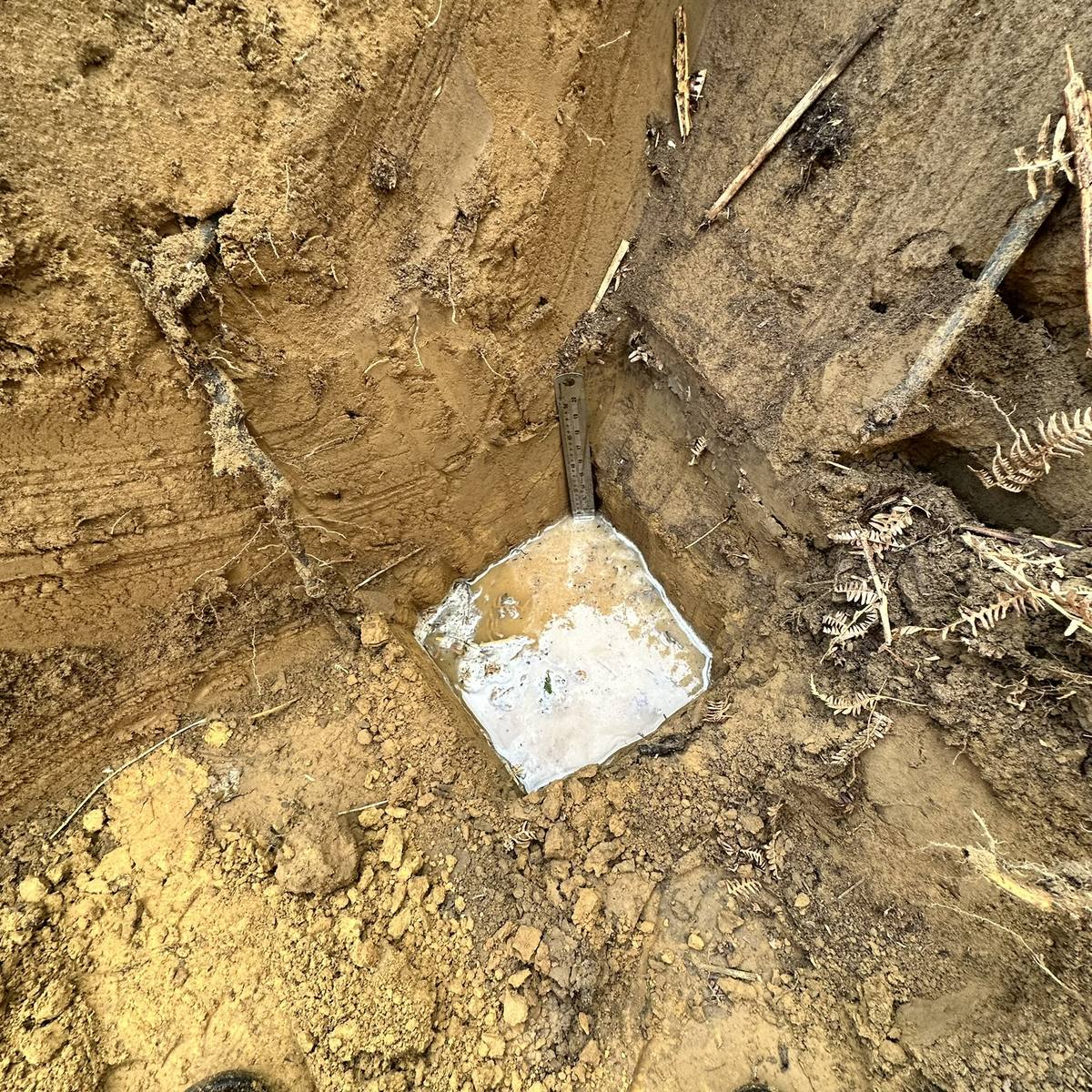 Square BS 6297 foul infiltration test hole filled with water, with a rule in place to measure the water level